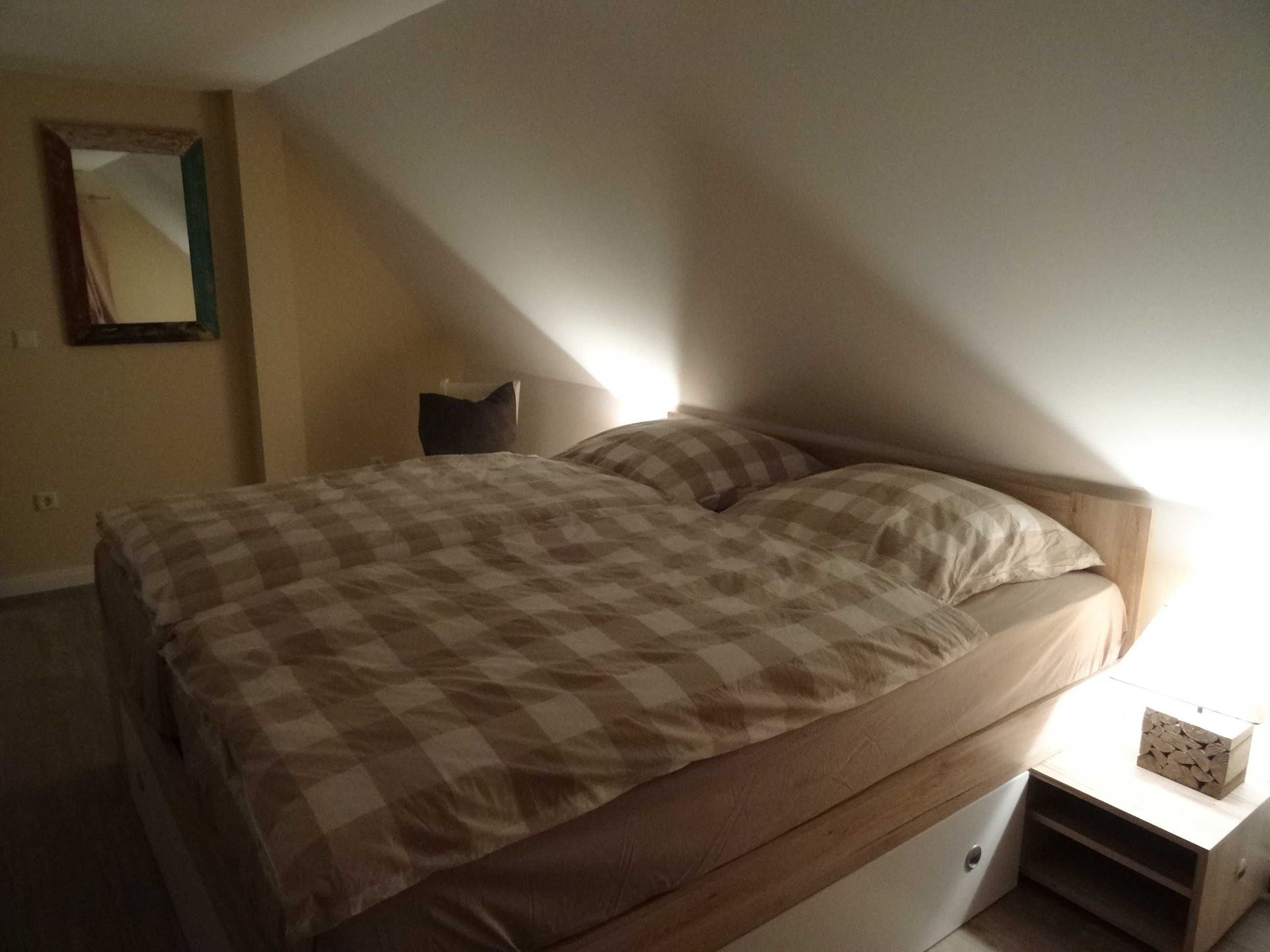 A bedroom with a bed, a nightstand, a mirror, and a wall-mounted shelf.
