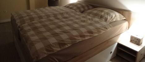 A bedroom with a bed, a nightstand, a mirror, and a wall-mounted shelf.