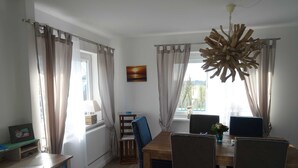 Ett matområde med ett träbord, stolar och en kristallkrona. Det finns gardiner vid fönstren och en tavla på väggen.