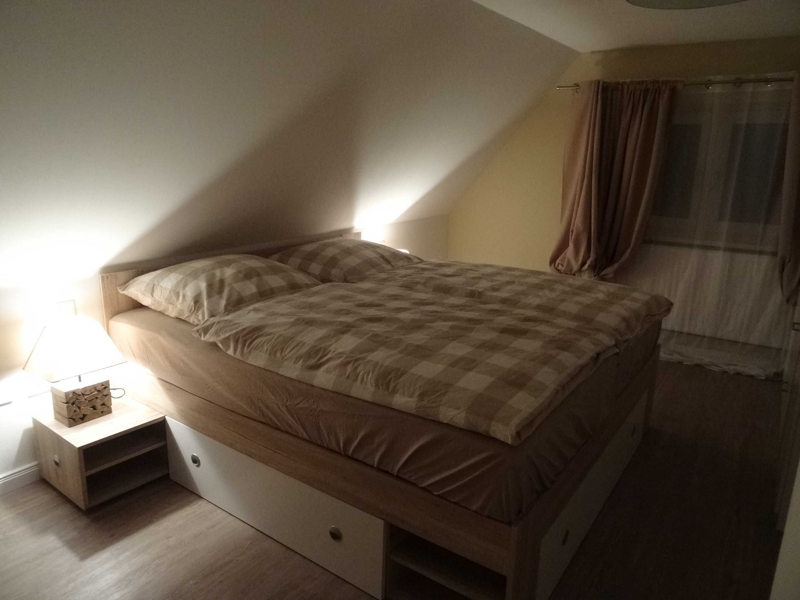 A bedroom with a bed, a nightstand, a lamp, and a window with curtains.