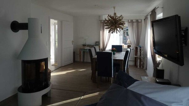 Ett modernt vardagsrum med en stor öppen spis, en matplats och en tv som är monterad på väggen.