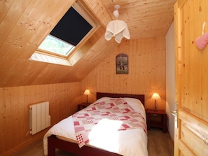 Um quarto acolhedor de madeira com teto inclinado, uma cama com colcha, duas luminárias de cabeceira e um radiador.