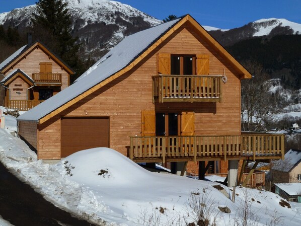 Een houten chalet met een balkon, met een besneeuwde berg op de achtergrond.