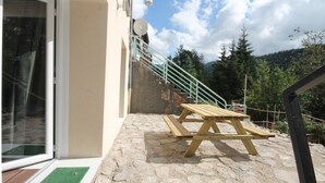 A stone patio with a wooden table and bench, a glass door, and a staircase leading to a higher level. - Mont-Dore T2 with West Terrace and Wi-Fi (Mont-Dore)