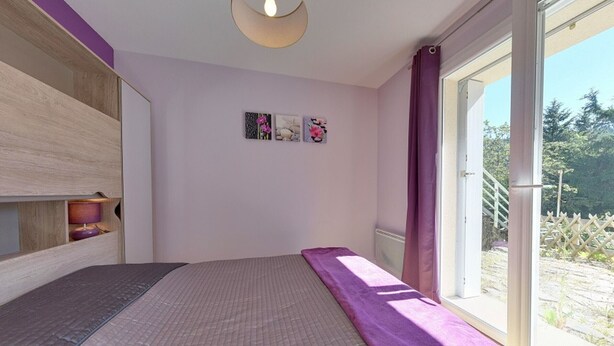 A bedroom with a bed, a window with curtains, a wall-mounted light, and a shelf with a lamp. - Mont-Dore T2 with West Terrace and Wi-Fi (Mont-Dore)