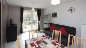 A modern living room with a sofa, a dining table with a quilt, a TV, and a view of the outdoors. - Mont-Dore T2 with West Terrace and Wi-Fi (Mont-Dore)