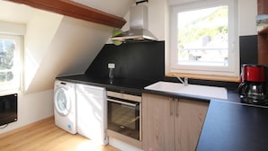 Ett kompakt kök med tvättmaskin, ugn och kaffebryggare.