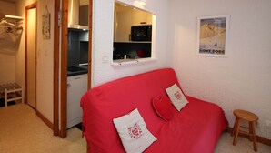A compact living space with a red sofa, a small stool, a kitchen area with a microwave, and a poster on the wall.