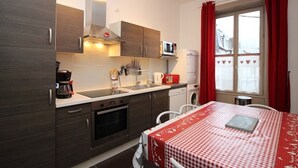A compact kitchen with dark wood cabinets, a microwave, a coffee maker, and a dishwasher. There's a dining area with a red and white checkered tablecloth and a window with red curtains.