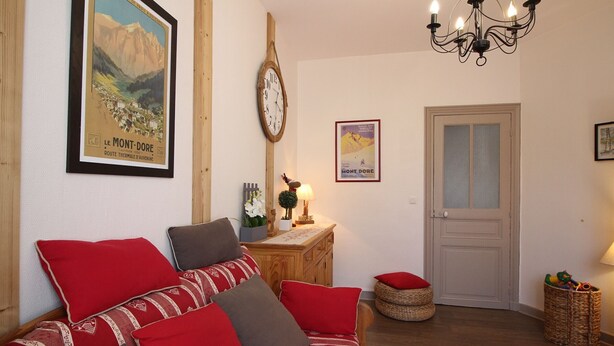 A cozy living room with a wooden sofa, a wall clock, a framed poster, and a door.