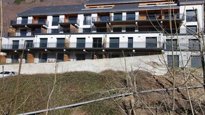 En flereetagers boligbygning med altaner, en betonfundament og en skråning i baggrunden.