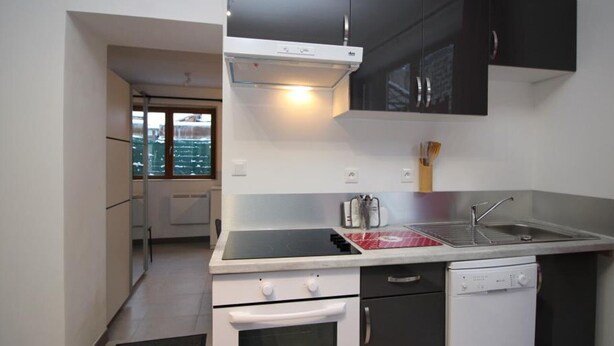 Cozinha compacta com fogão, forno, lava-louças e janela com vista para a cidade.