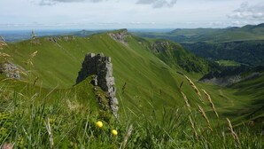 Paisagem montanhosa com uma formação rochosa em destaque no primeiro plano e vista de colinas ondulantes ao longe.