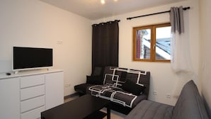 Uma sala de estar moderna com televisão de tela plana, um sofá, uma mesa de centro e uma janela com cortinas.