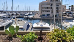 Uma marina com vários barcos atracados, um edifício com varandas e um céu claro.