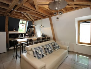 A modern kitchen with wooden beams, a dining area with a sofa, and a large window. - Beautiful Duplex T3 in Mont-Dore with Parking, Near the Thermal Baths (Mont-Dore)