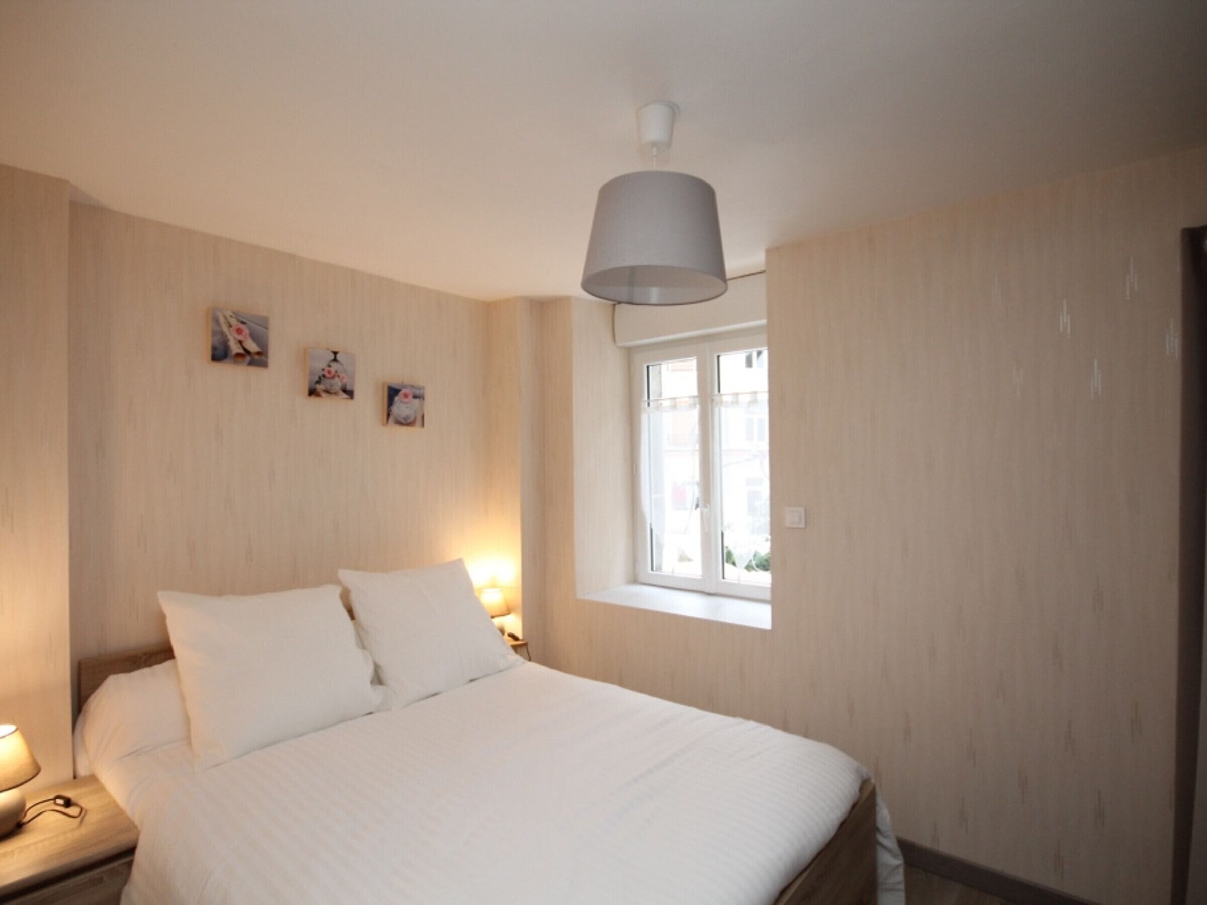 A bedroom with a bed, bedside lamps, a window, and wall-mounted artwork.