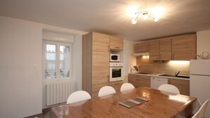 A modern kitchen with wooden cabinets, a dining table with chairs, and a built-in oven.