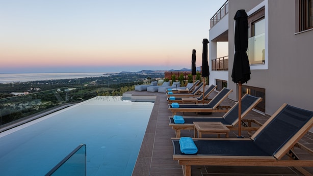 Piscina infinita en la azotea con sillones de descanso y sombrillas, con vistas a un paisaje pintoresco.