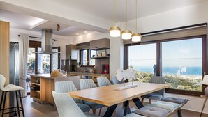 Una cocina moderna con una isla central, comedor con bancos y amplios ventanales que ofrecen vista al mar.