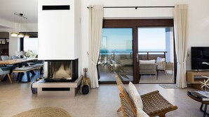 Una sala de estar moderna con chimenea, zona de estar y vistas al océano a través de amplios ventanales.