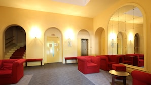 Un'hall con posti a sedere rossi, una scala e un grande specchio che riflette l'ambiente.