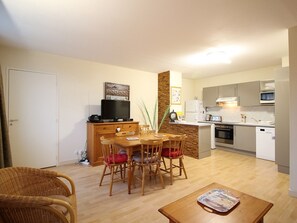 Un espacio habitable compacto con comedor, kitchenette y televisor sobre un mueble de madera.