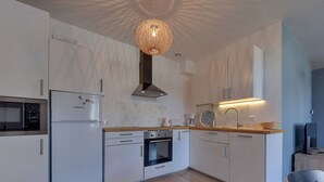 A modern kitchen with white cabinetry, a built-in oven, a microwave, and a hanging light fixture. - T3 Apartment in La Bourboule Center with Balcony and Small Dog Allowed (La Bourboule)