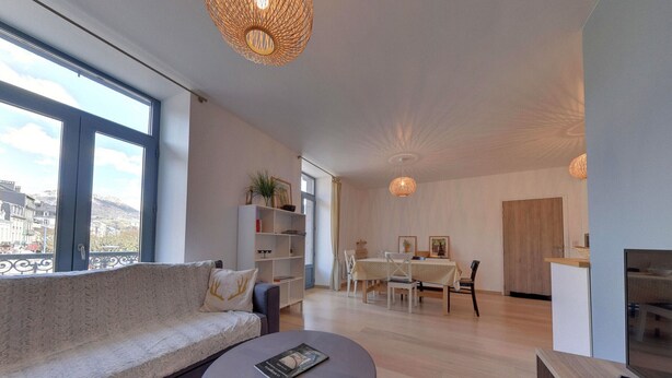 A modern living room with a sofa, a small round table, and a dining area with a table and chairs. - T3 Apartment in La Bourboule Center with Balcony and Small Dog Allowed (La Bourboule)