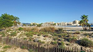 A coastal view with a sandy beach, palm trees, and a row of buildings in the background.