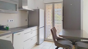 A modern kitchen with a built-in microwave, a stainless steel refrigerator, and a dining area with a table and chairs.