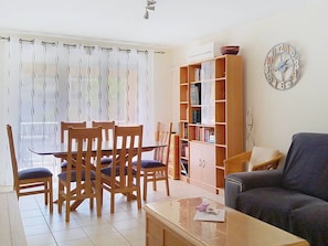 Un salon comprenant une table à manger, des chaises, un canapé, une bibliothèque et une horloge murale.
