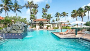 A swimming pool with a rock feature, lounge chairs, and palm trees.