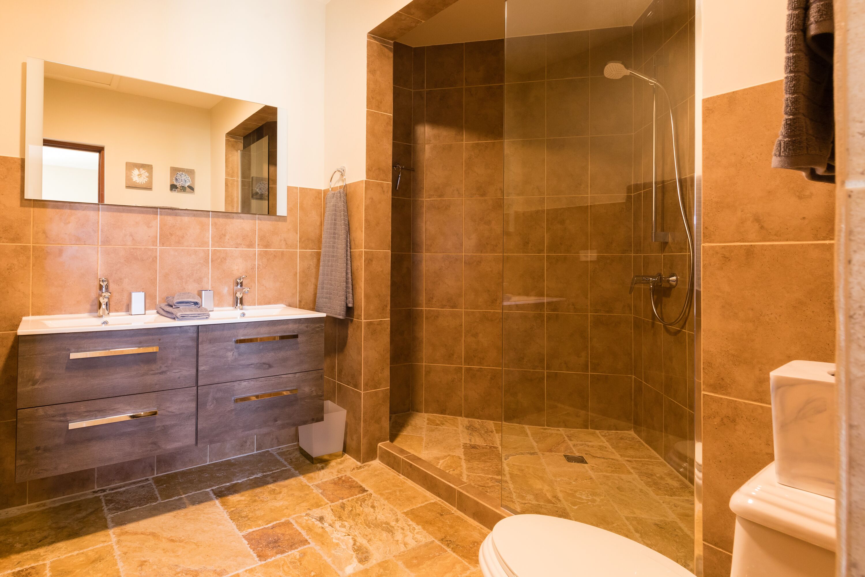 Een badkamer met douche, toilet en wastafel met lades en een spiegel.