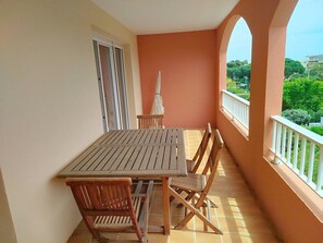Ein Balkon mit Holztisch und -stühlen, einem weißen Sonnenschirm und Blick auf Grünflächen und Gebäude.