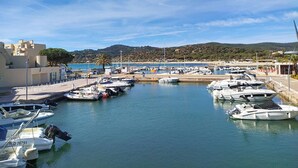 Una marina con barcos amarrados, cielo despejado y un paisaje montañoso al fondo.