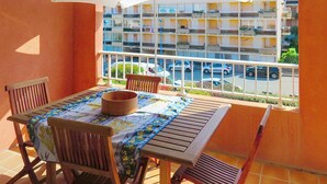 Un balcón con mesa y sillas, un paraguas grande, y vista a un edificio de varios pisos con balcones.