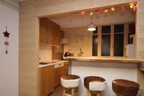 Une cuisine avec des meubles de rangement en bois, un plan de travail et deux tabourets dotés d’assises en fourrure.
