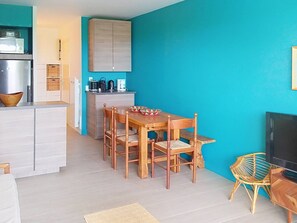 A compact kitchen with a dining area, a TV, and a wicker chair.