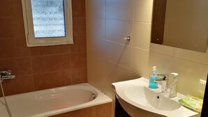 A bathroom with a bathtub, toilet, sink, and a window. - Beach House (artemida)