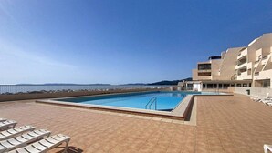 Una piscina en la azotea con sillones, vista despejada al mar y un edificio moderno con balcones.