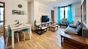A living room with a dining table, chairs, a TV, a sofa, and a coffee table. - La Bourboule: Comfortable T3, Parking, WiFi (La Bourboule)