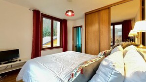 A bedroom with a bed, a TV, a window, and a wardrobe. - La Bourboule: Comfortable T3, Parking, WiFi (La Bourboule)