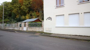 A two-story building with a stone facade, a small attached garage, and a metal fence. - La Bourboule: Comfortable T3, Parking, WiFi (La Bourboule)