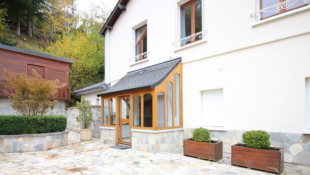A stone-paved courtyard with a wooden door and windows, surrounded by stone walls and potted plants. - La Bourboule: Comfortable T3, Parking, WiFi (La Bourboule)