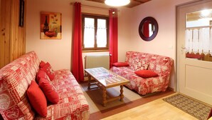 A cozy room with two patterned sofas, a wooden table, a mirror, and a window with red curtains. - Chalet 6 rooms, sleeps 8, near center, WIFI (Mont-Dore)