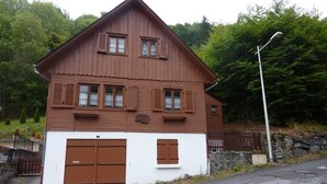 A two-story wooden house with a white lower section, featuring a garage and two windows with shutters. - Chalet 6 rooms, sleeps 8, near center, WIFI (Mont-Dore)