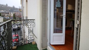 Un balcón con barandilla metálica, un coche rojo estacionado afuera y una puerta que da a un espacio interior con piso de baldosas y un adorno navideño.