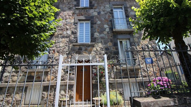 A stone building with a gated entrance, a wooden door, and a balcony. - Bright apartment in La Bourboule, 3 bedrooms, near center (La Bourboule)