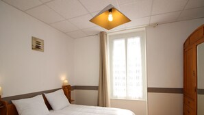 A bedroom with a bed, a nightstand, a wooden wardrobe, and a window with curtains. - Bright apartment in La Bourboule, 3 bedrooms, near center (La Bourboule)